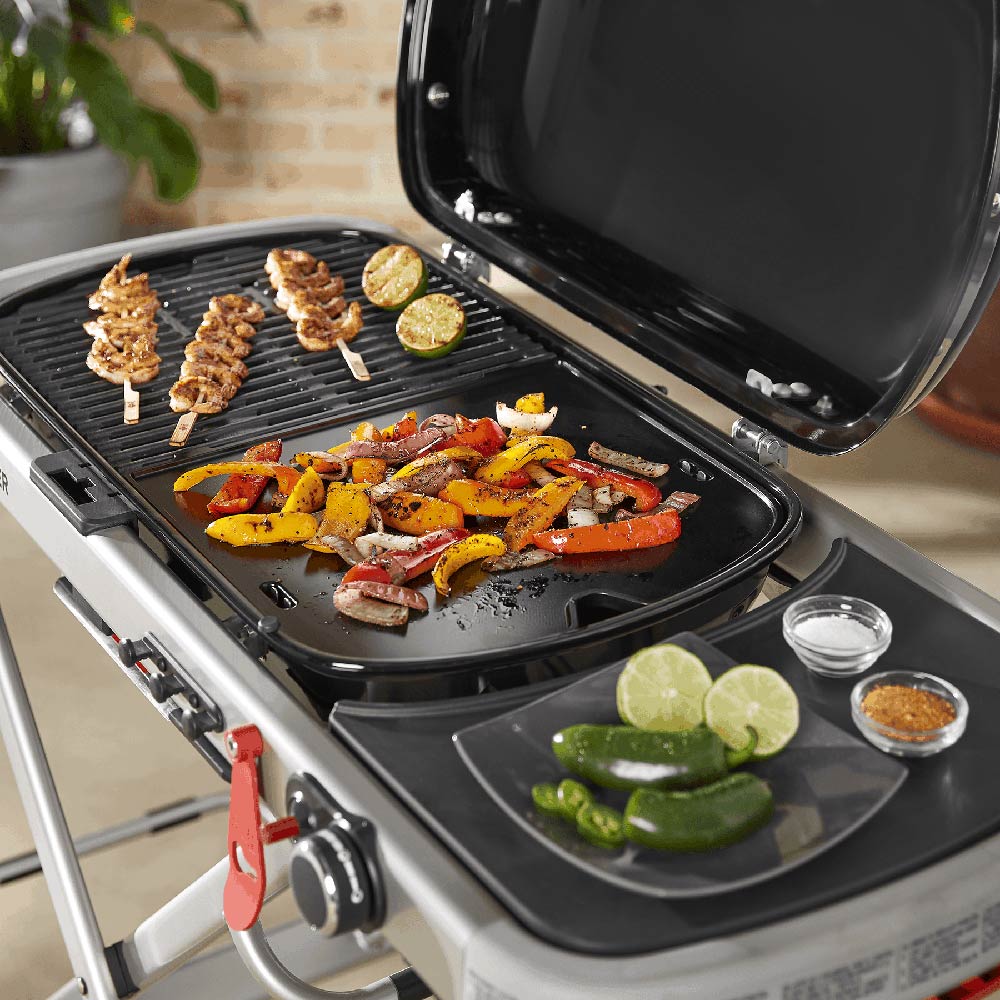 Black griddle plate insert open on Traveler grill, with food cooking
