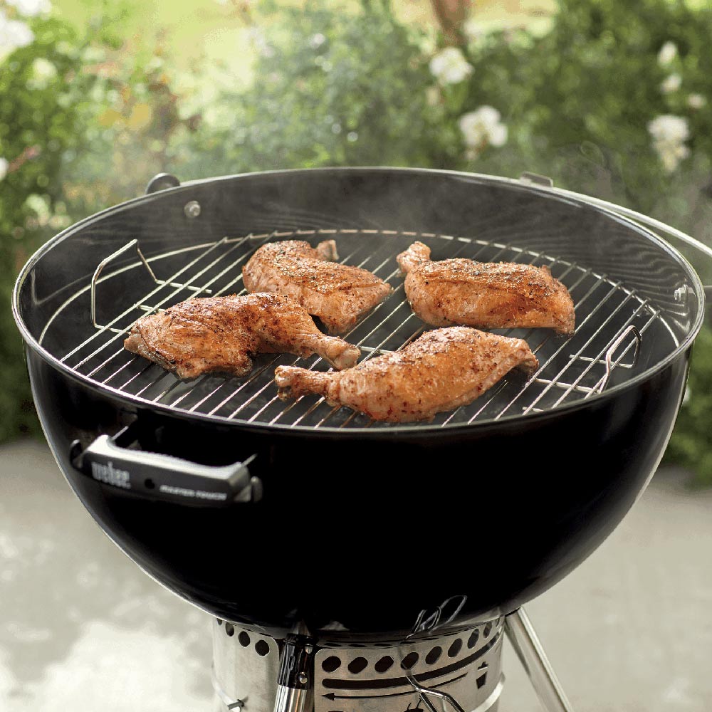 Weber charcoal grill cooking grate with several seasoned chicken pieces on wires