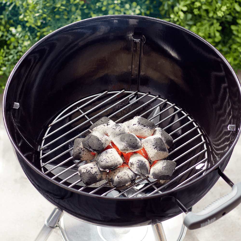 Round metal charcoal grate holding scattered charcoal pieces inside a grill.