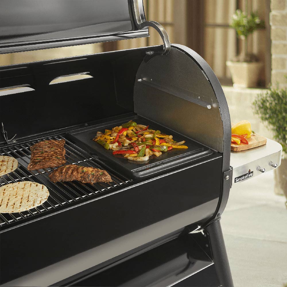 Outdoor grill with griddle plate, with cooked meat and diced vegetables on black grates
