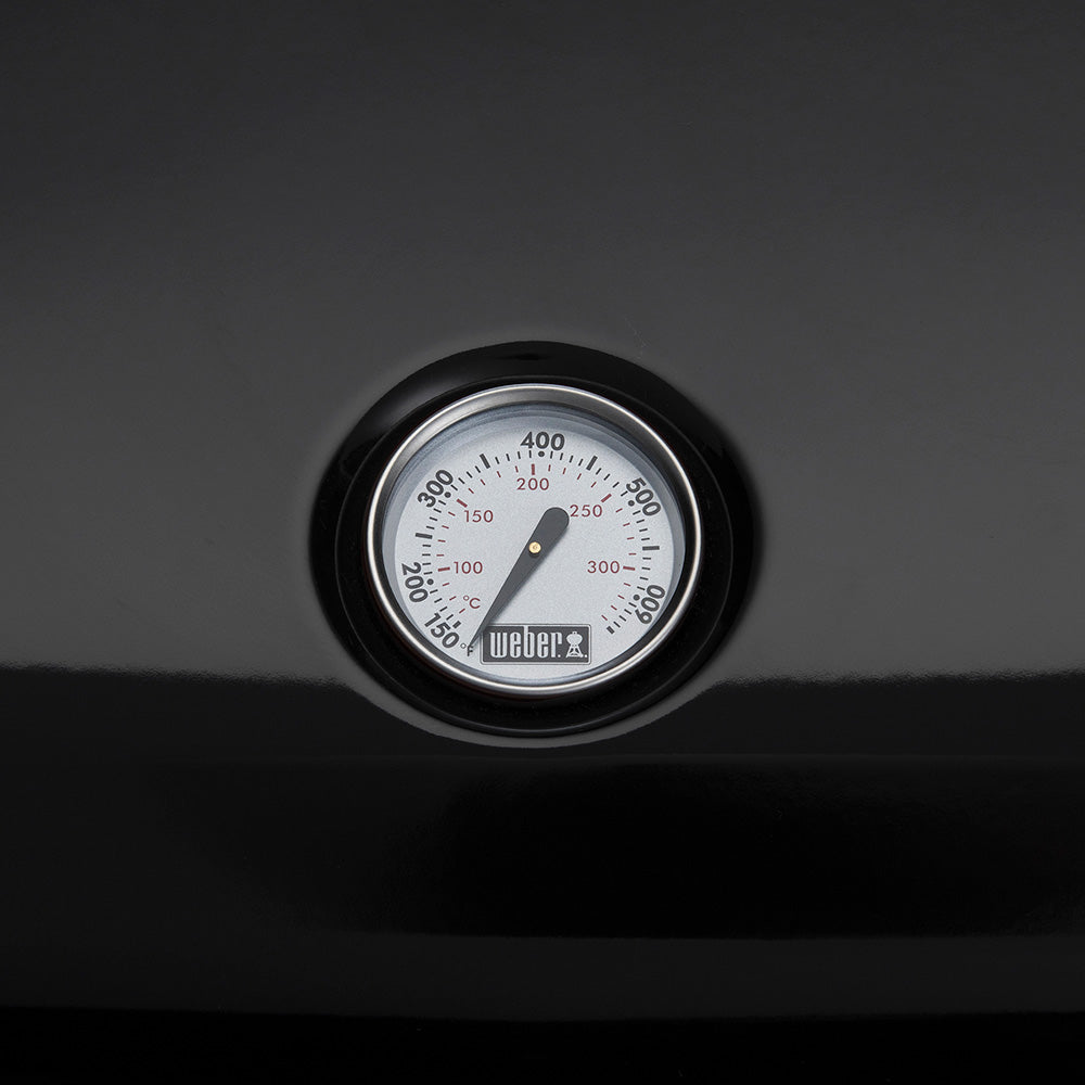Black grill thermometer dial with temperature scale and Weber logo.