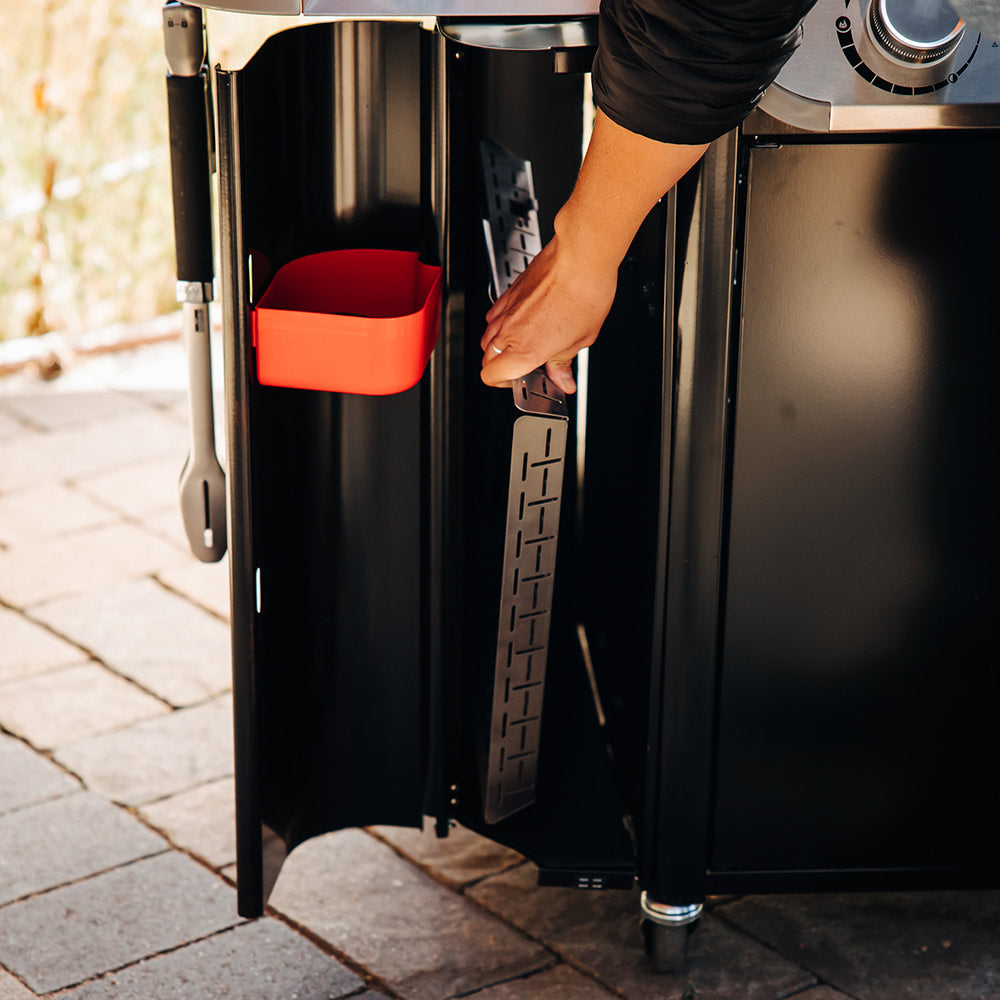 Black grill side compartment with a red pull-out tray and storage door