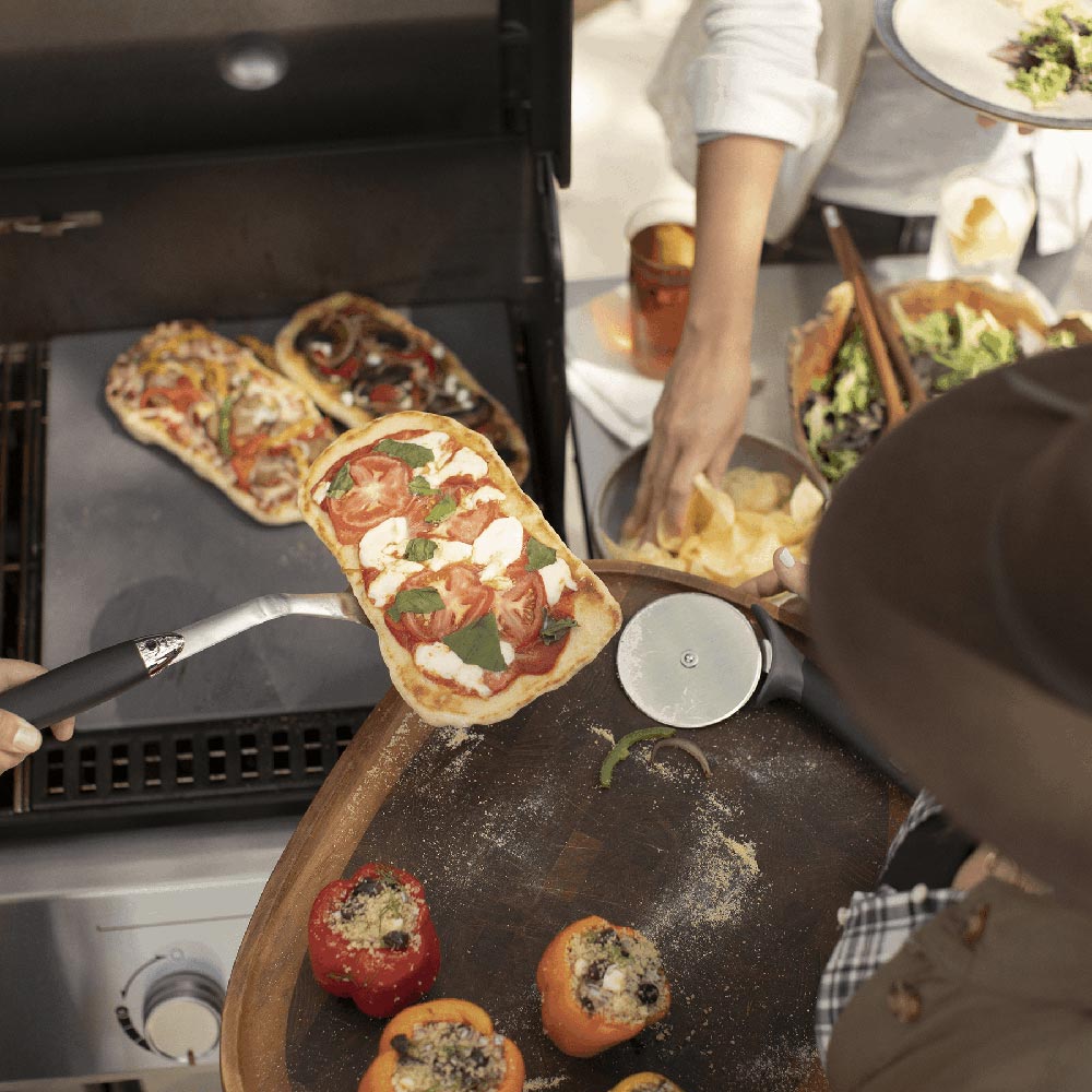 Gas grill cooking surface with pizza on a stone inside the open grill