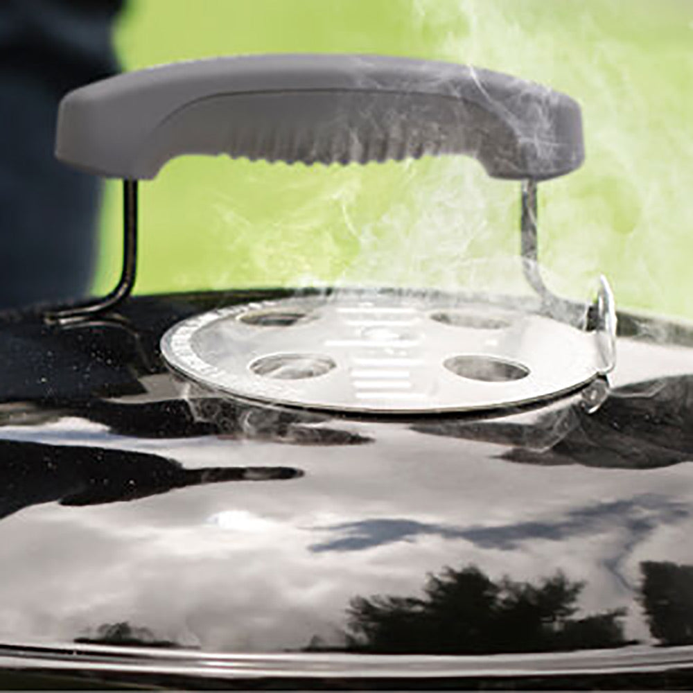 Charcoal grill lid vent plate with handle, lid open over the cooking area.