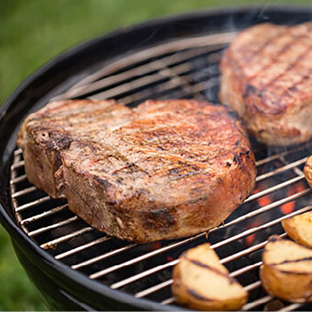 Charcoal grill with seared steaks and sliced vegetables on the cooking grate.
