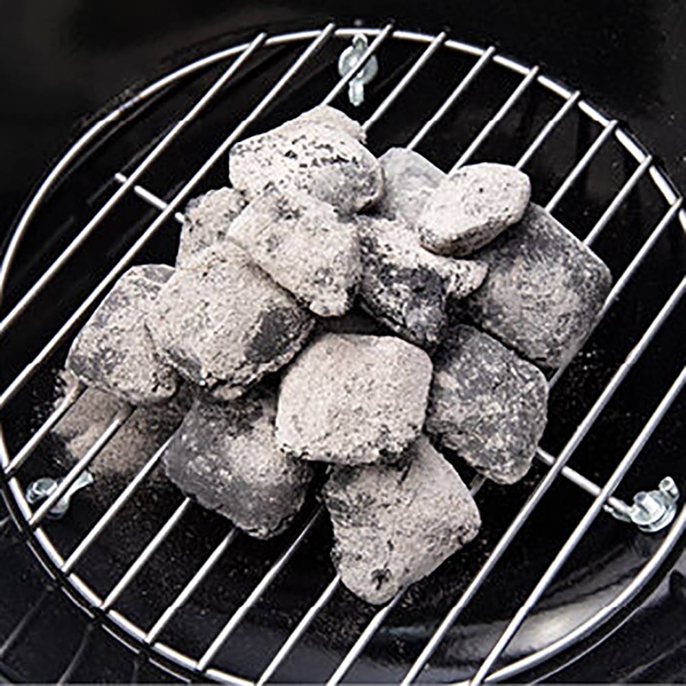 Charcoal briquettes burning on the grill grate inside a black dome charcoal grill.