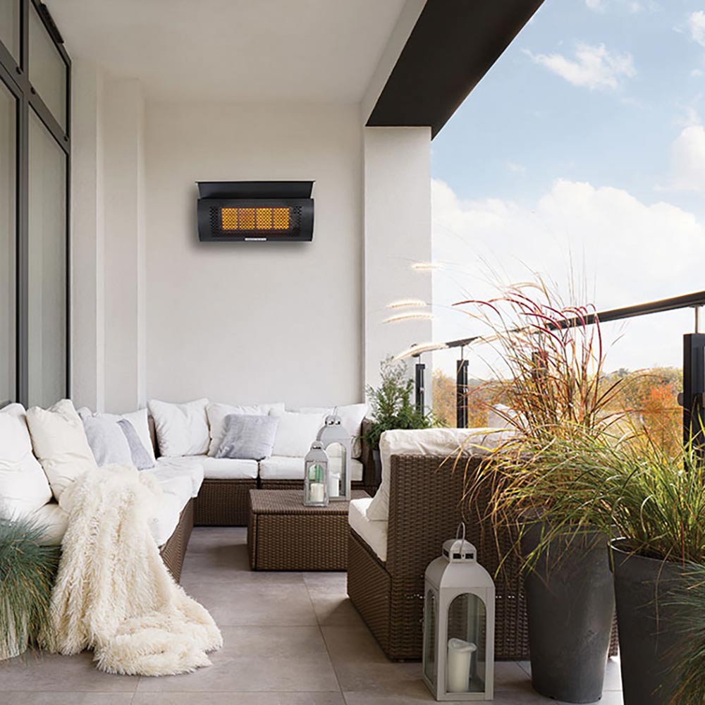 Wall mounted infrared heater with glowing orange heating panel on a white patio wall