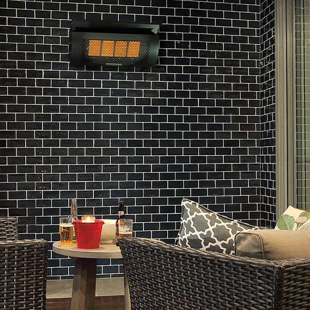 Infrared wall heater with glowing orange panel mounted on a dark brick wall