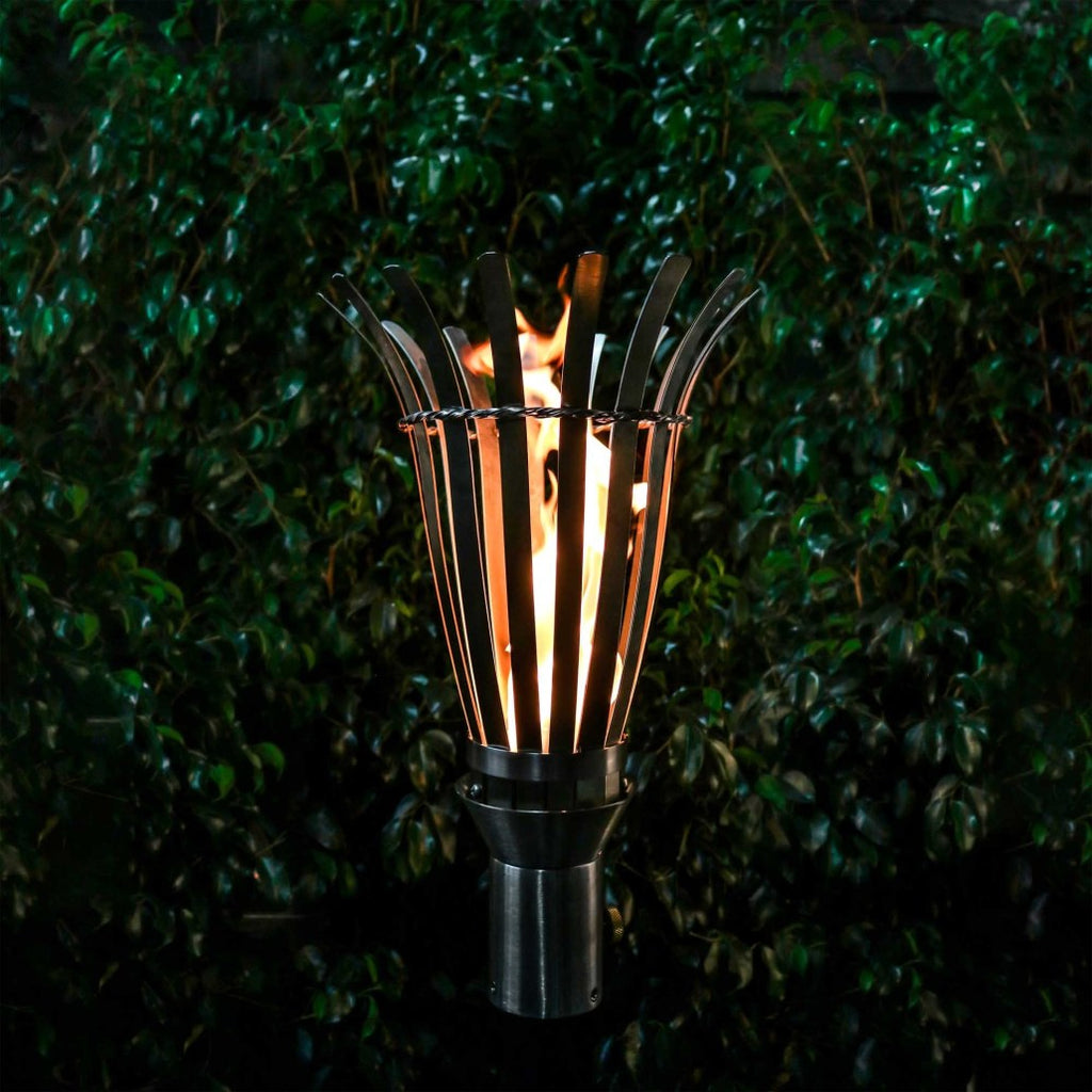 Outdoor torch with black basket and metal rods surrounding a flame, on a stand