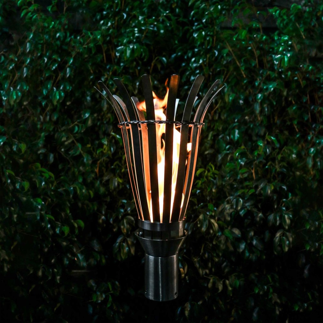 Outdoor torch with black basket and metal rods surrounding a flame, on a stand