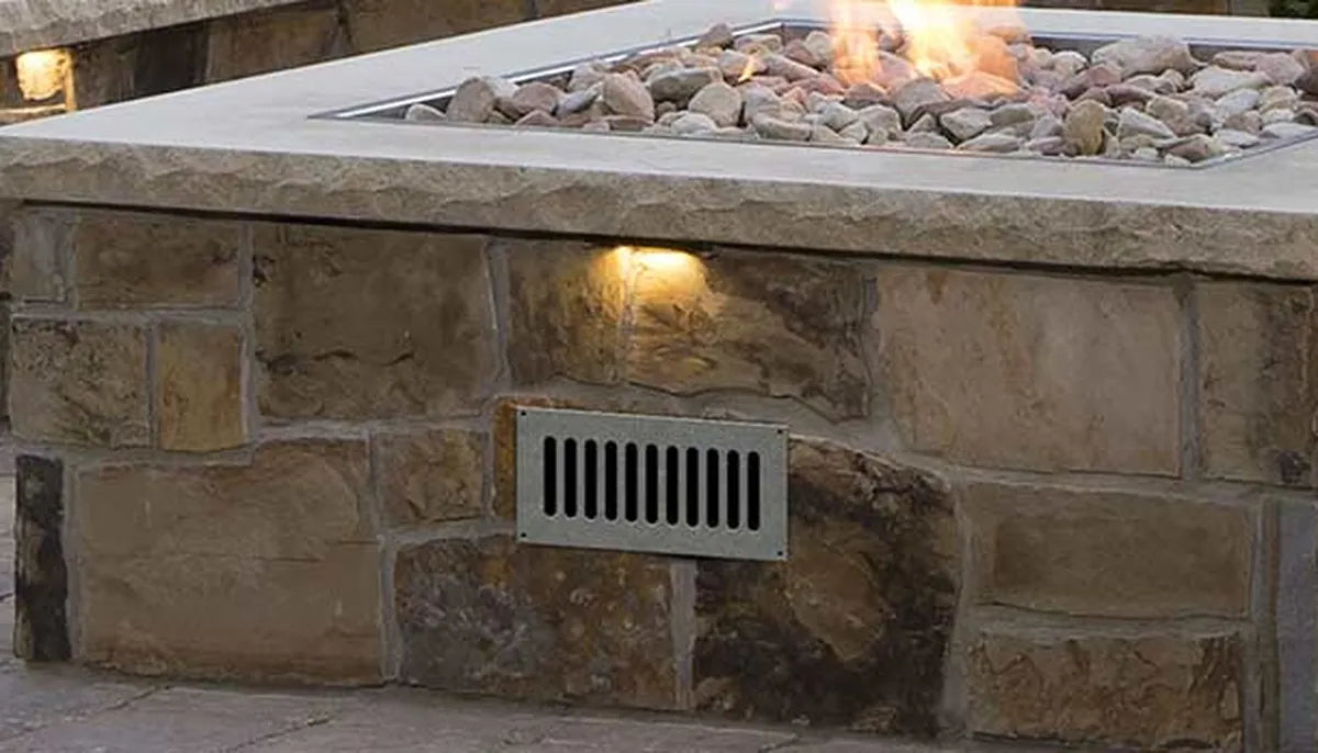 Square natural stone fire pit with stainless vent grate and lit burner — fire pit ventilation and airflow design