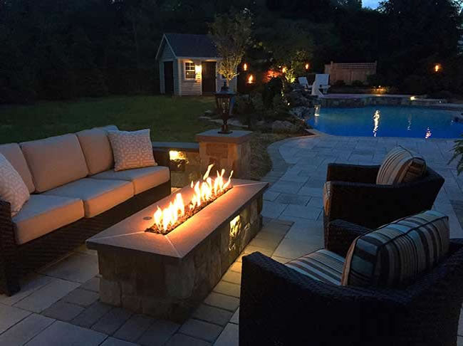Outdoor rectangular fire pit with flames and dark stone surround on patio