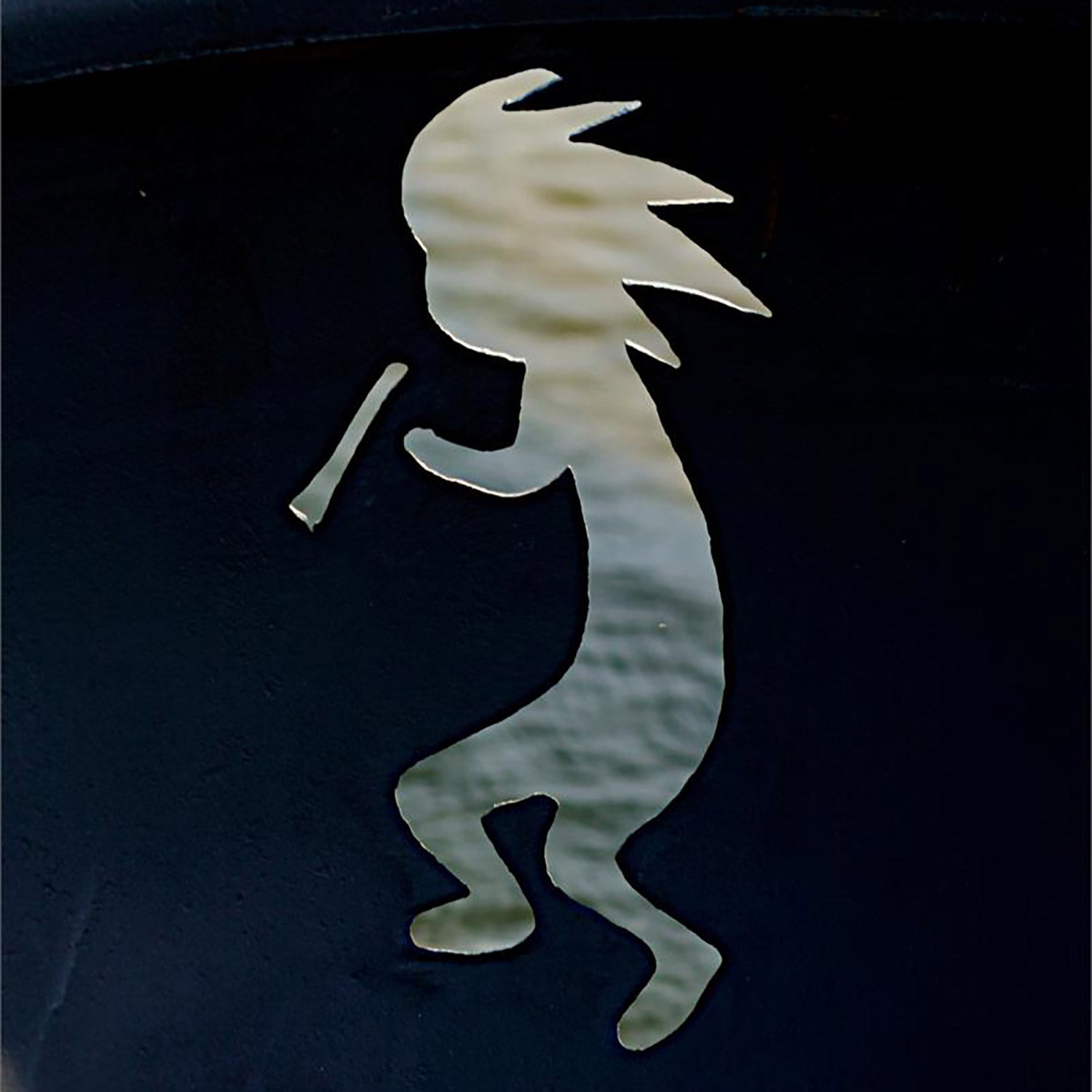 Close-up of Kokopelli metal cutout on dark fire pit bowl