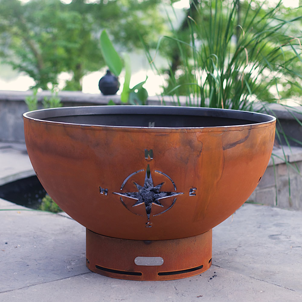 Rust gas fire pit bowl with star compass emblem and blue flame visible inside