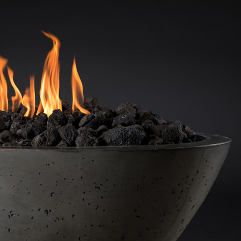 Corner view of an oval fire pit bowl with flames and black lava rocks, speckled gray