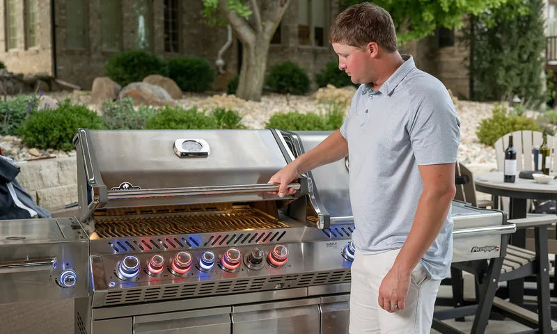 Man inspecting a premium Napoleon stainless steel gas grill with illuminated burner knobs in a backyard setting