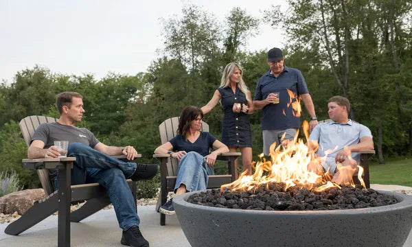Five friends relaxing around a glowing Spotix fire pit bowl in Adirondack chairs on a backyard patio at evening