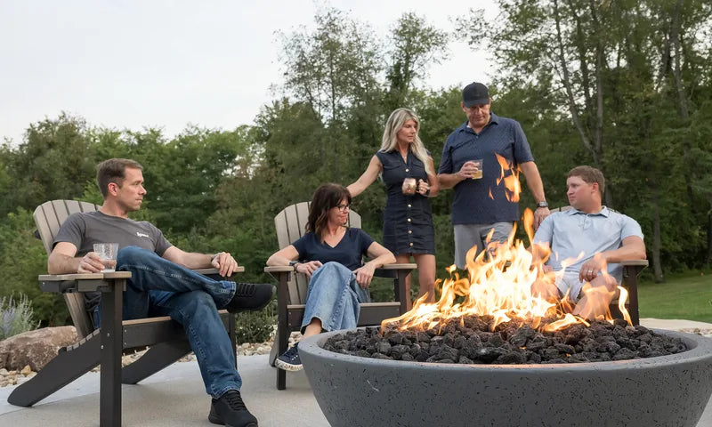 Five friends relaxing around a glowing Spotix fire pit bowl in Adirondack chairs on a backyard patio at evening